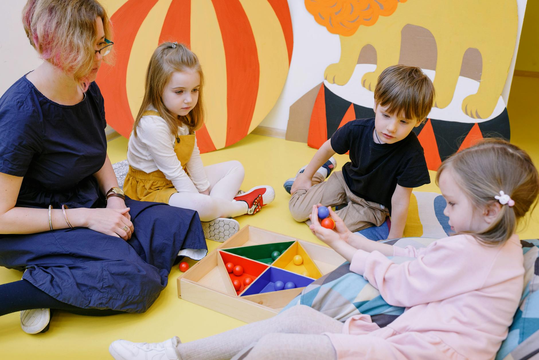 A teacher kneeling to take notes on a clipboard while observing a young child stack colorful rings.