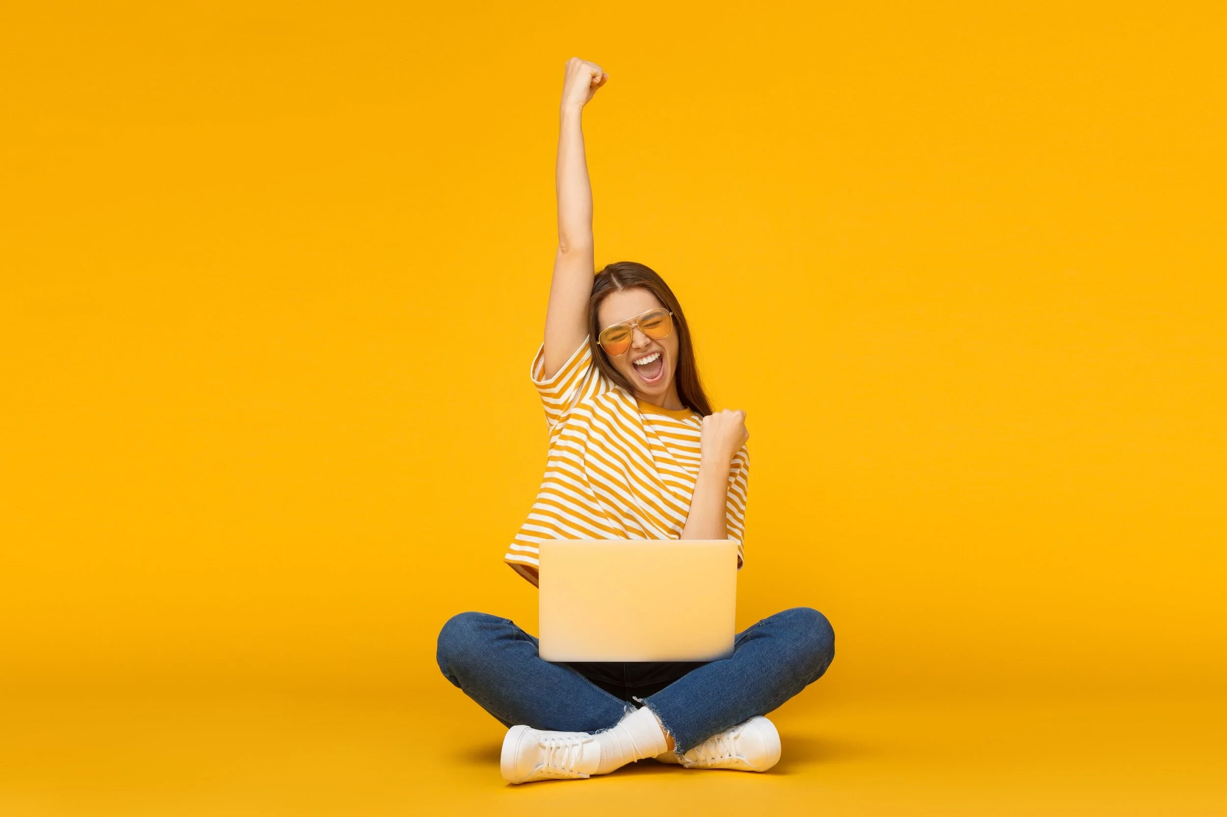 Woman cheering by laptop against yellow wall