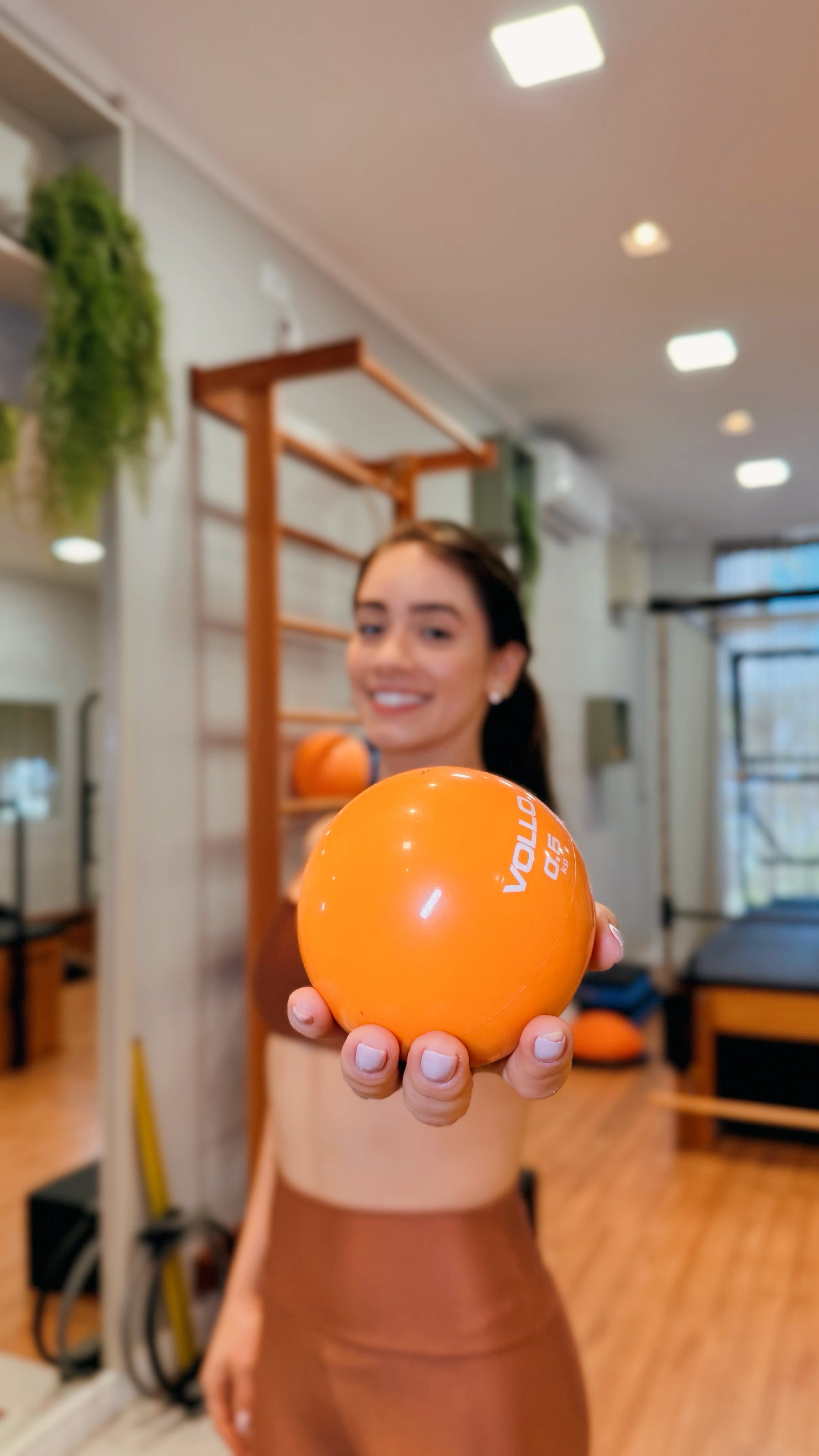 Doutora da equipe Addere segurando bola de pilates laranja de 65cm no estúdio da clínica em Maringá
