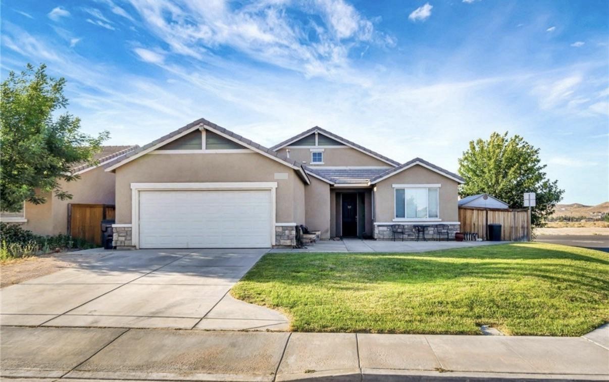 Original desert stucco home — tan walls, green gable siding, white garage door, grass lawn