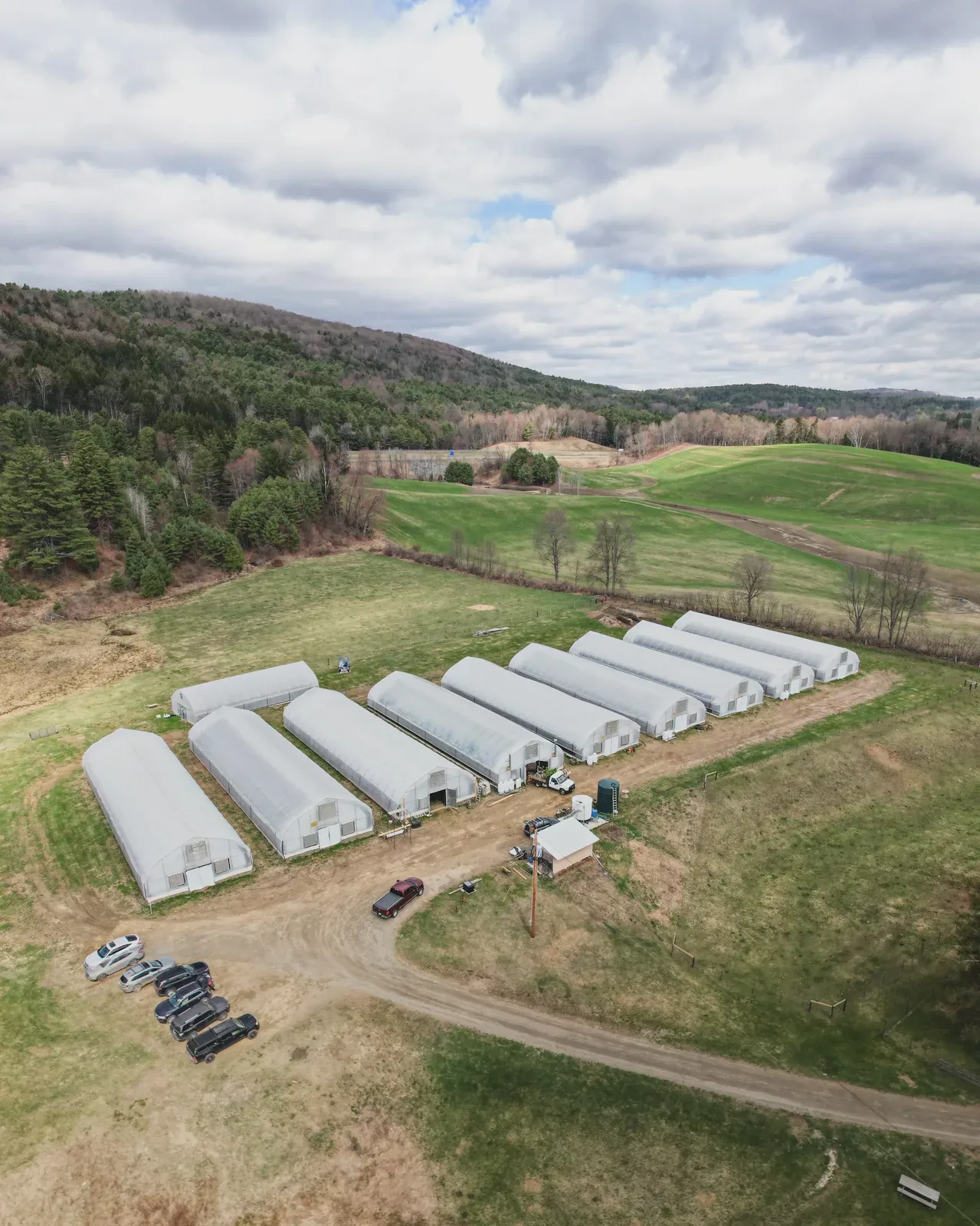 Aerial view of Sunkissed Farm's full greenhouse complex surrounded by Vermont hillside pastures and forest, a 29-acre living soil cannabis operation in Windsor