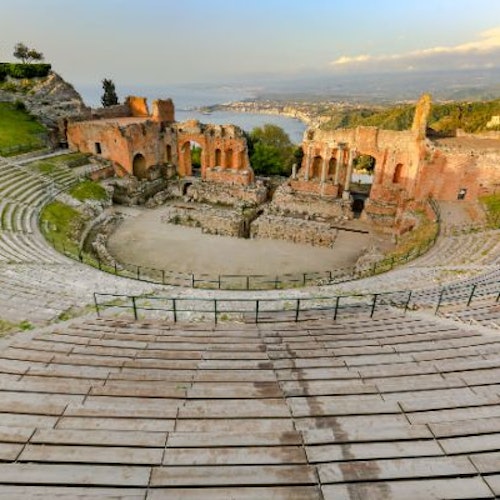 Un ancien amphithéâtre avec des sièges en pierre, surplombant des ruines et un paysage côtier lointain sous un ciel partiellement nuageux.