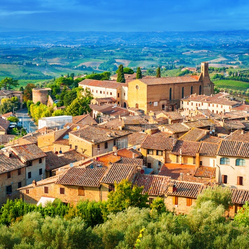 俯瞰一个中世纪小镇，陶土色屋顶的建筑物、一座突出的石头教堂，以及周围郁郁葱葱的乡村。