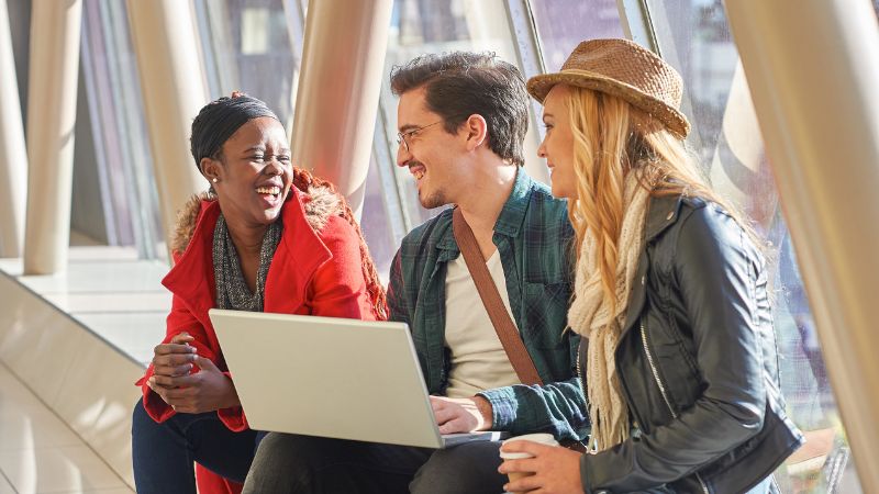 People talking and holding a laptop at an outdoor event.