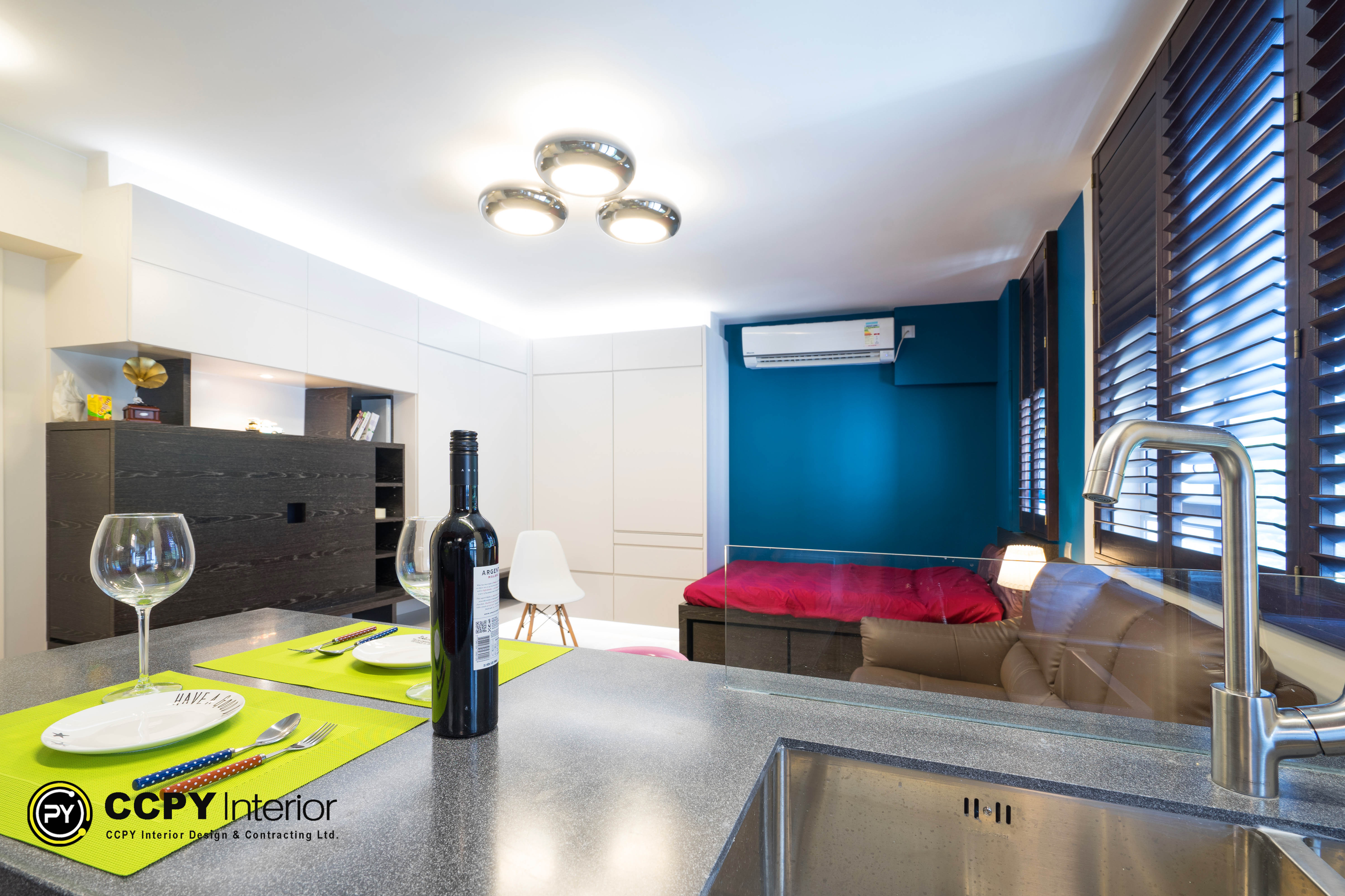 The interior design project by CCPY Interior features a contemporary, smart luxury theme in a modern studio apartment. Key aspects include space optimization with an open-plan layout, integrated low-profile furniture, and reflective surfaces that enhance light. The intelligent lighting incorporates recessed ceiling lights and a multi-ring fixture, while the color palette blends neutral tones with vibrant accents. Bespoke cabinetry adds functionality with a sleek, minimal design, complemented by warm accents like a vintage gramophone, creating a high-fashion contrast in aesthetics.