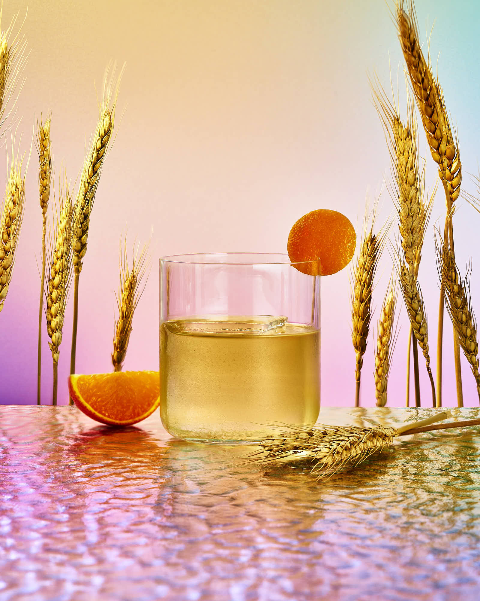 A glass of golden liquid sits on a colorful surface with decorative elements and a simple orange ornament.