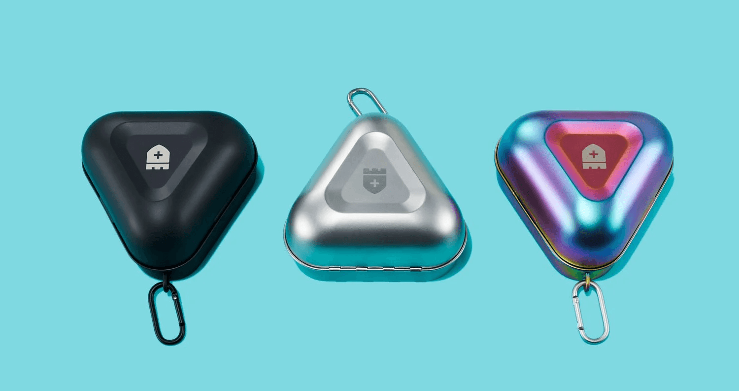 Three CastleGrade triangular devices in black, silver, and iridescent finishes on a blue background