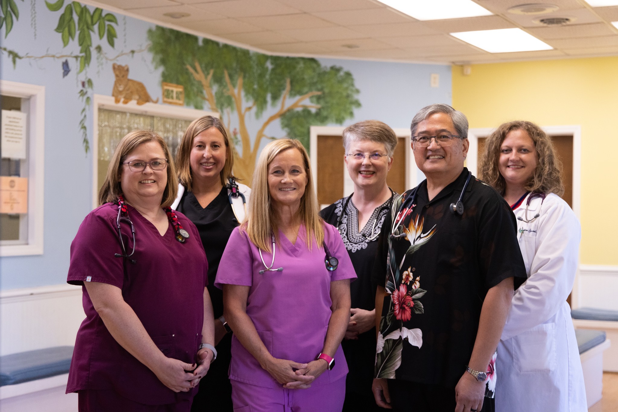 Team of six Pediatricians and Nurse Practitioners smiling in the lobby.