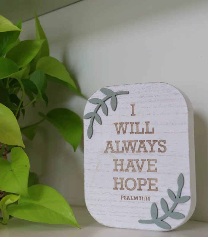 Decorative wall sign reading ‘I will always have hope’ beside green plant leaves.