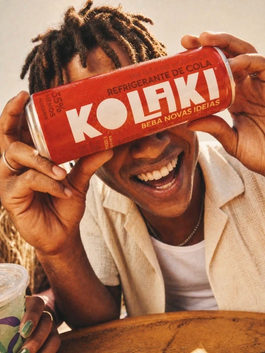 Jovem sorrindo segurando uma lata de Kolaki na frente do rosto