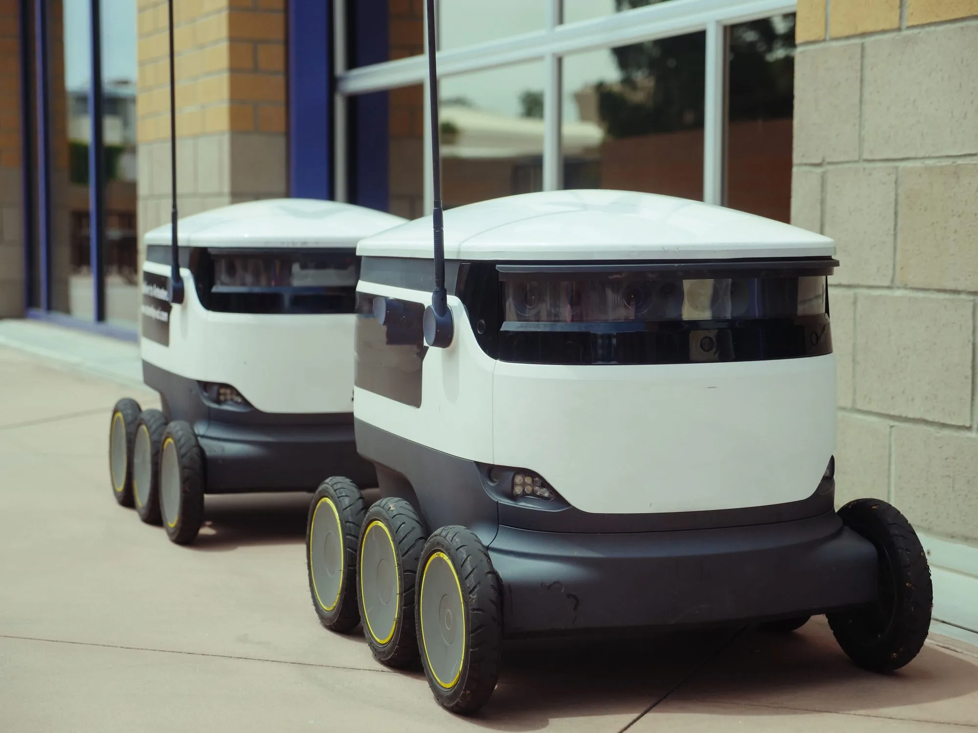 Two autonomous delivery robots travelling outside a building