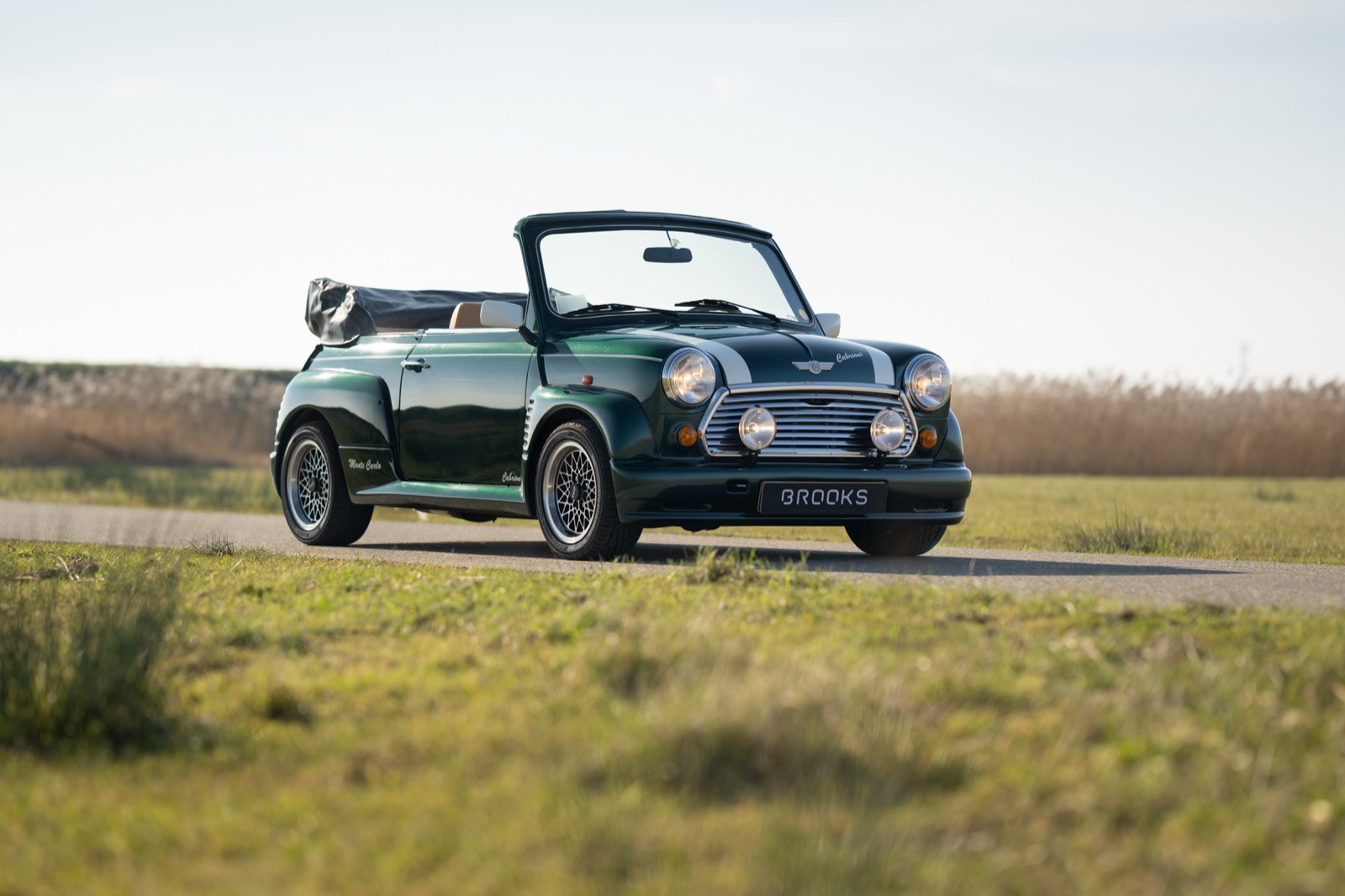 A convertible car parked on a dirt road surrounded by open fields under a clear sky.