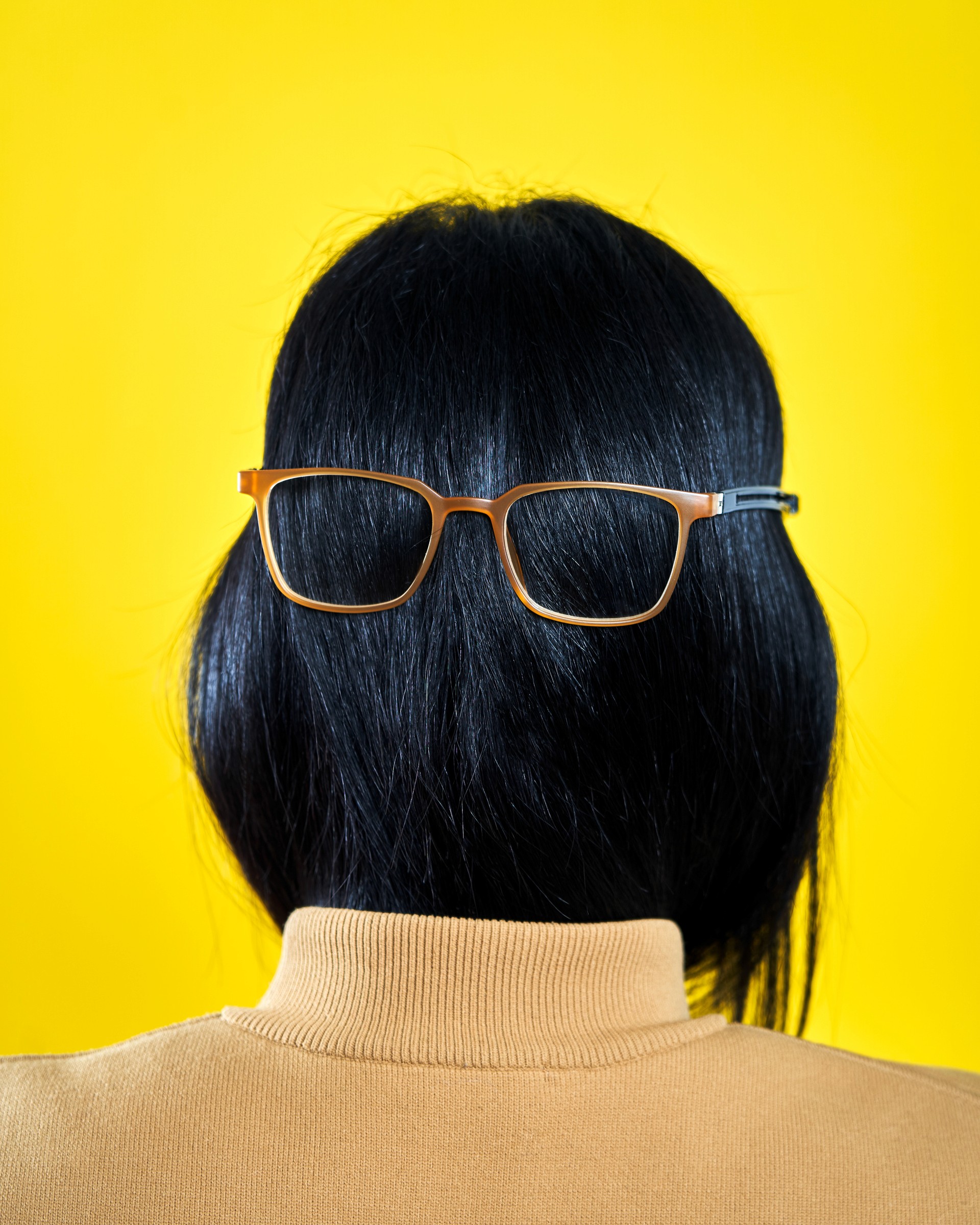 Photographie au flash d'un portrait de femme vu de dos avec des cheveux noirs portant des lunettes de lecture beige à l'envers