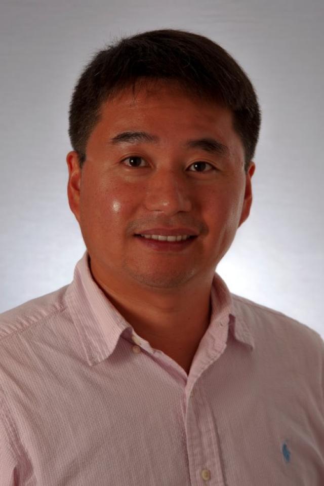 Portrait of a smiling Asian man wearing a pink collared shirt. He looks directly at the camera with a friendly expression.