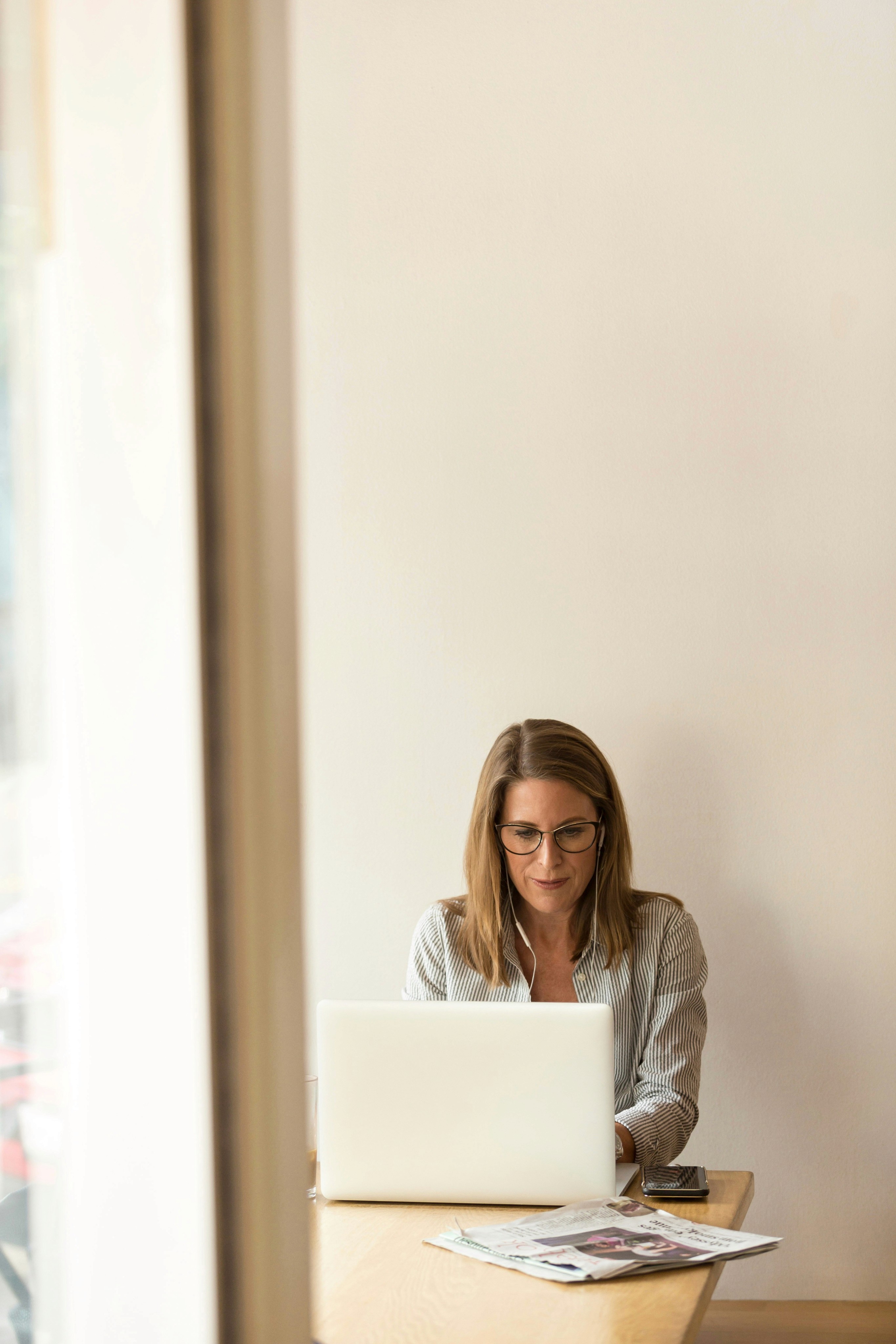  Woman sitting at a table using a computer, news paper on the table.