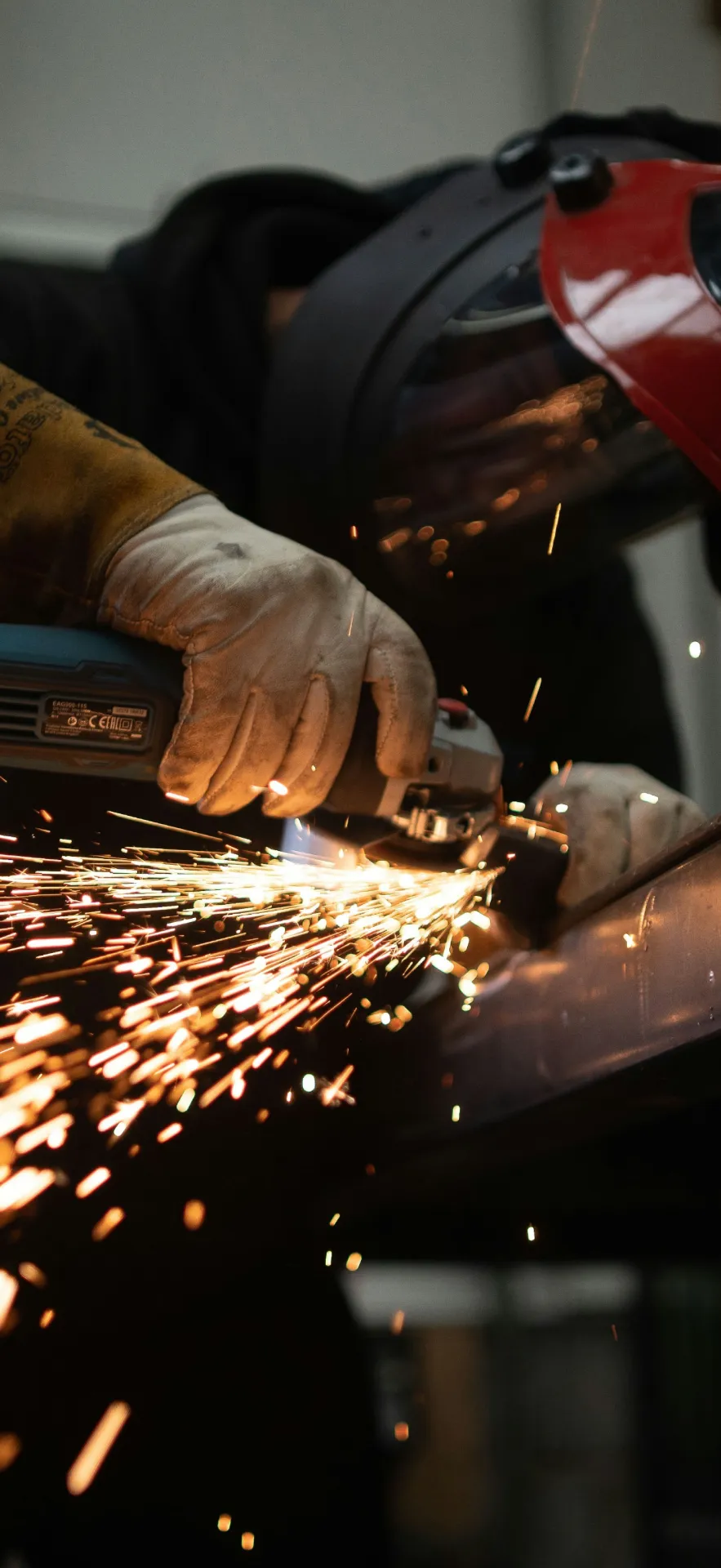 Steel fabrication process with worker grinding structural beam, producing sparks during metal finishing operation