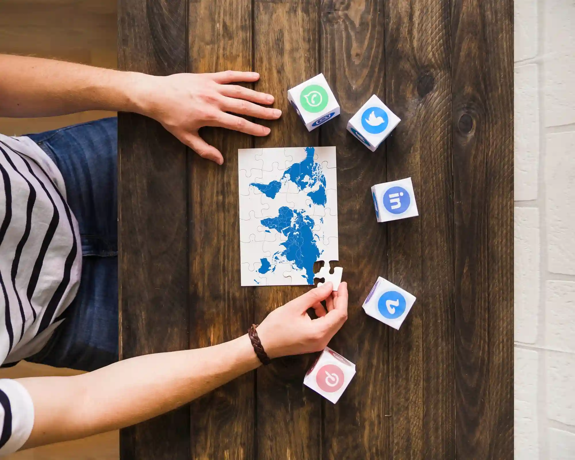 Person assembling a world map puzzle next to cubes displaying various social media platform logos.
