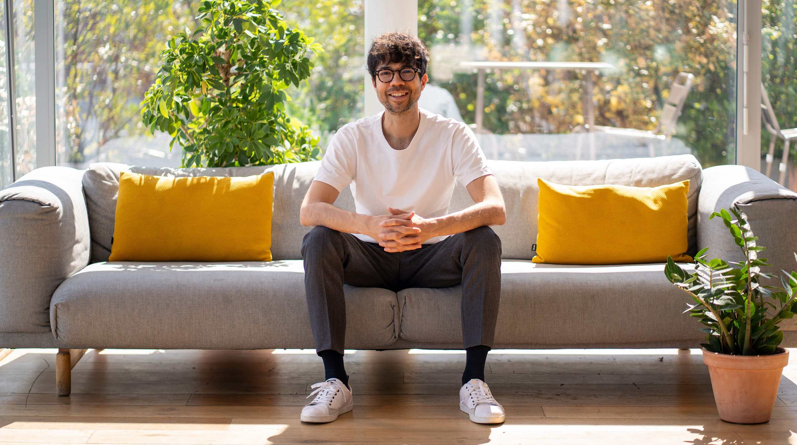 Jean-Charles, the man who made this website, sitting in a sofa, looking at you, smiling