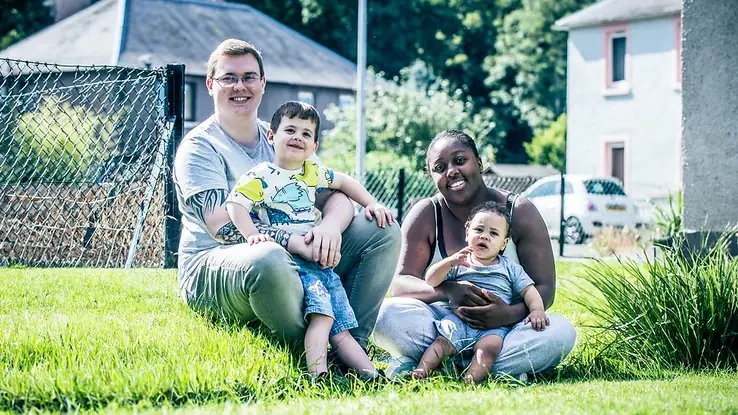 Family sitting together on a grassy lawn in a residential community setting.