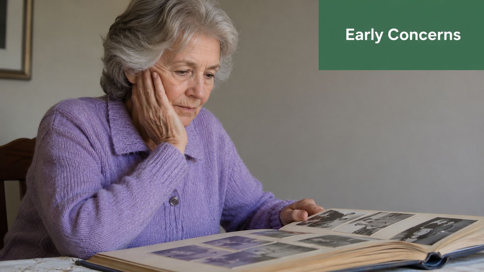 An elderly woman sitting thoughtfully while looking at an old photo album, appearing concerned and pensive.