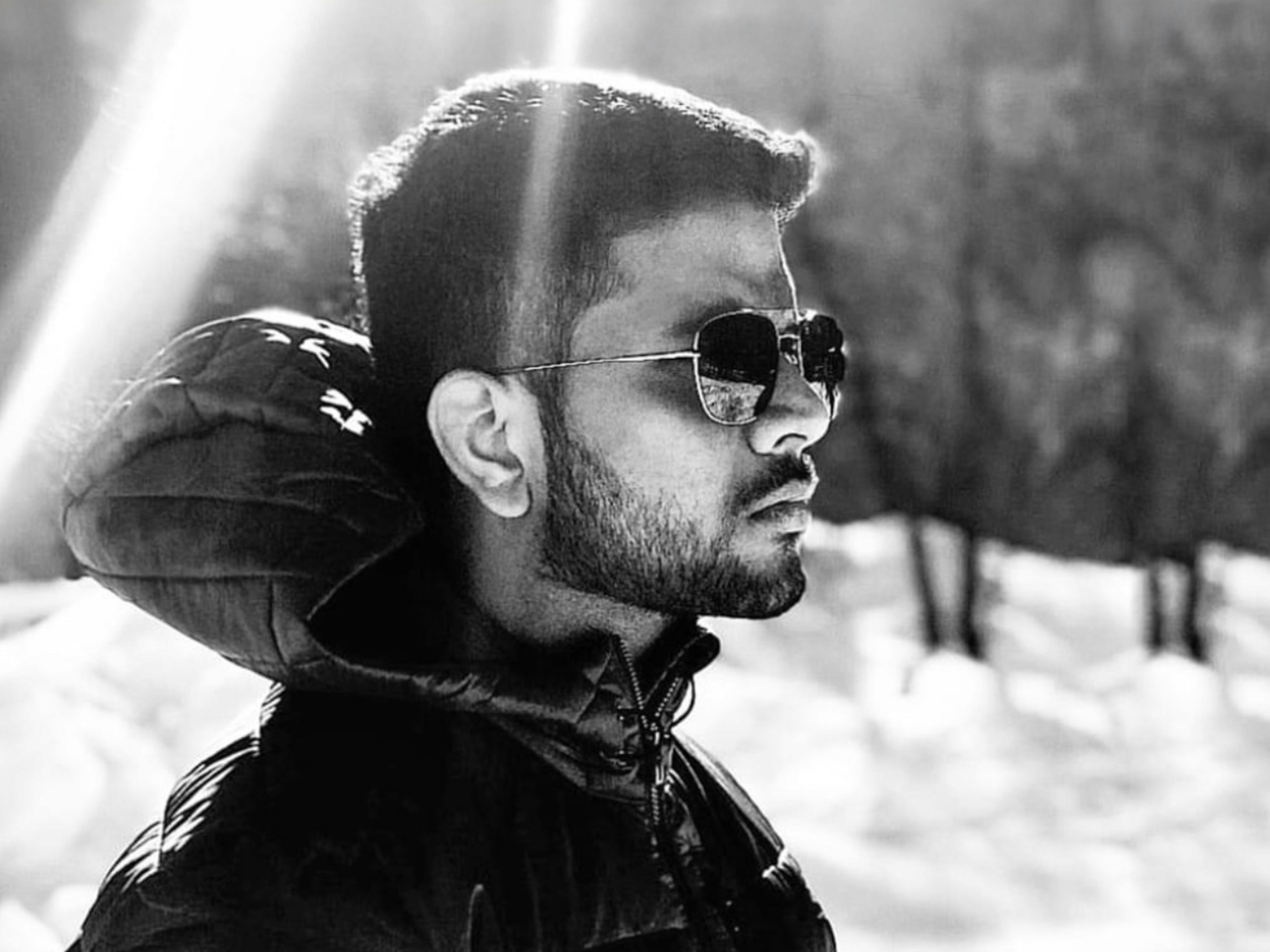 Woman with a short haircut smiling confidently, wearing a blazer and standing in warm natural light with modern architecture behind her.