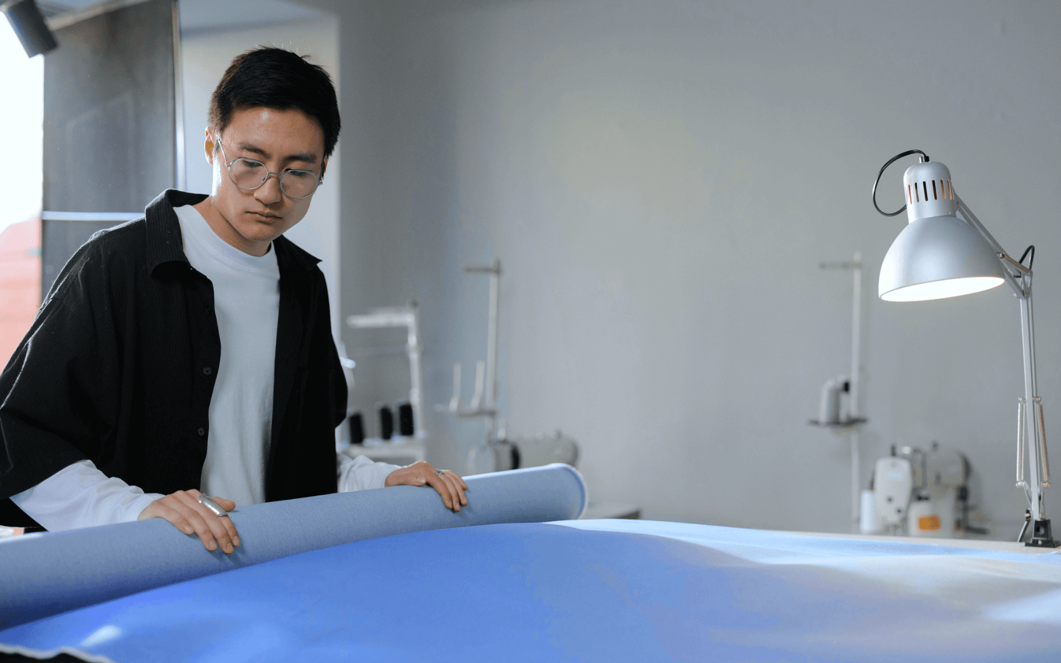 alt="man with roll of fabric in a studio"