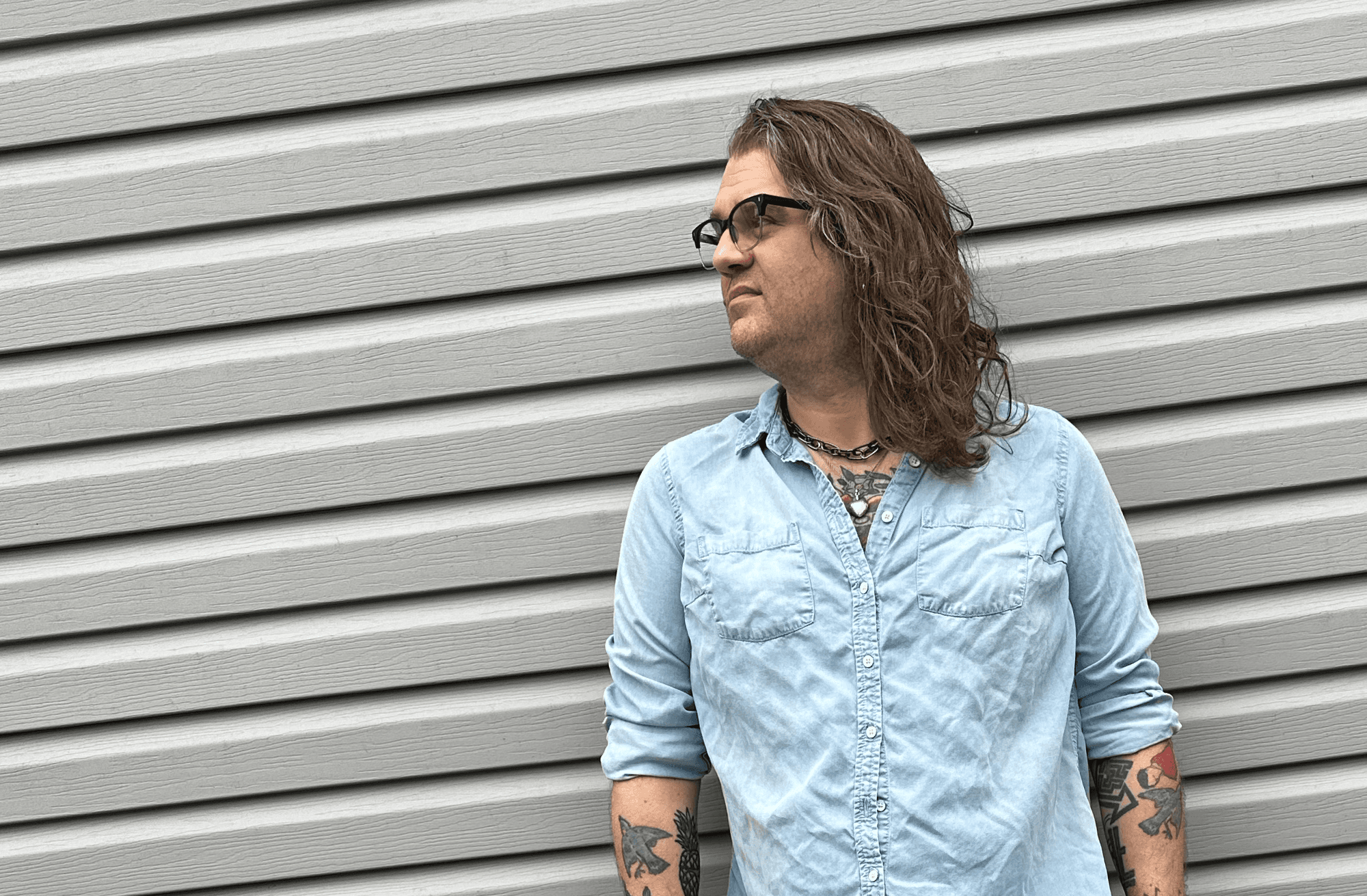 A half-length shot of Jane, wearing a denim button-up shirt against a backdrop of vinyl siding