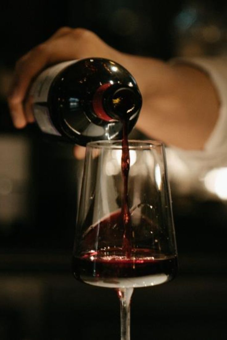 Une main verse du vin rouge dans un verre