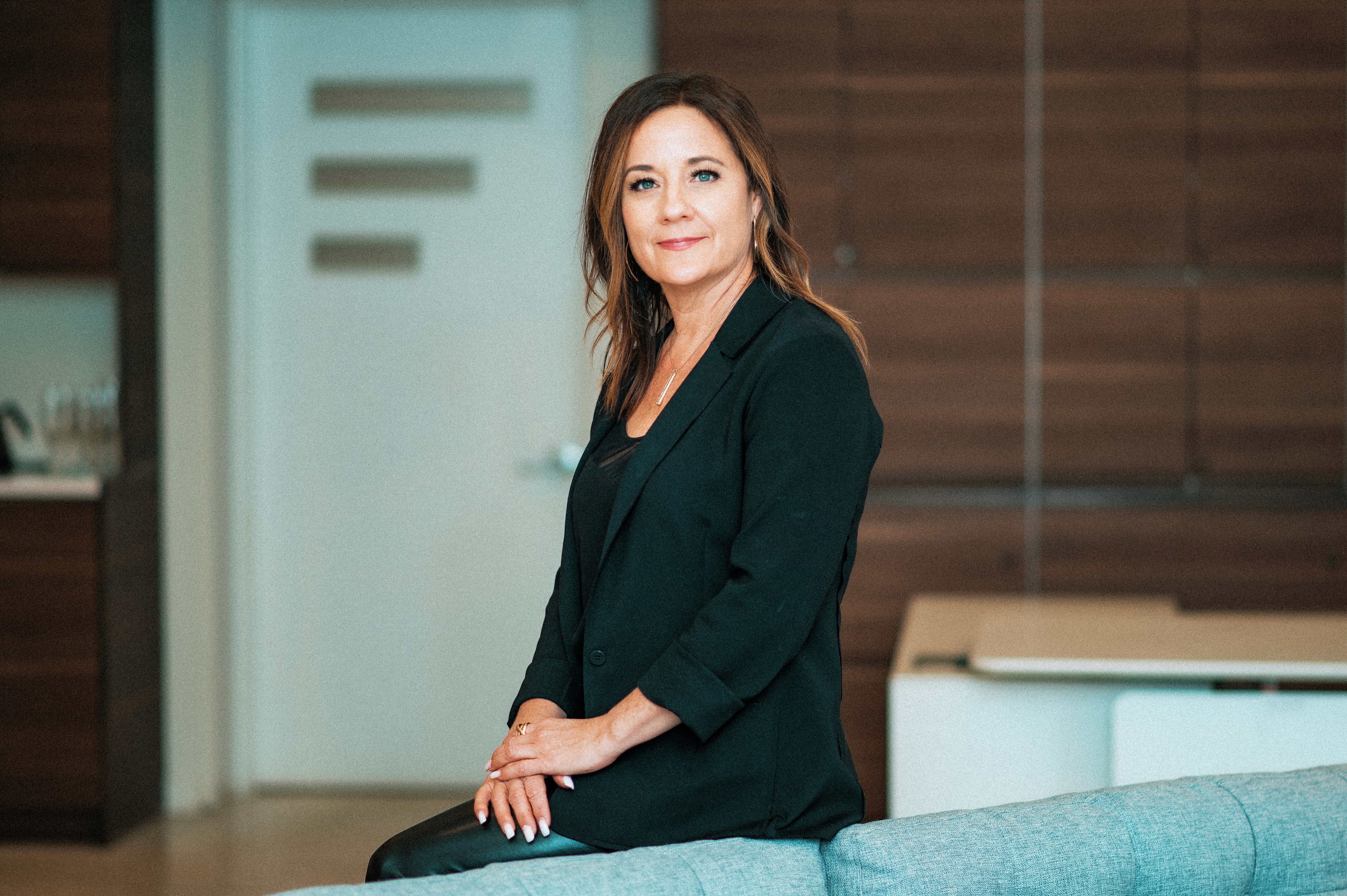 Cozy reading nook with sofa, chair, and plants inside a glass cabin with mountain forest views.