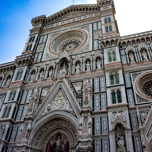 Вишуканий фасад собору з оздобленими скульптурами, вікнами-розами та детальним різьбленням під блакитним небом.