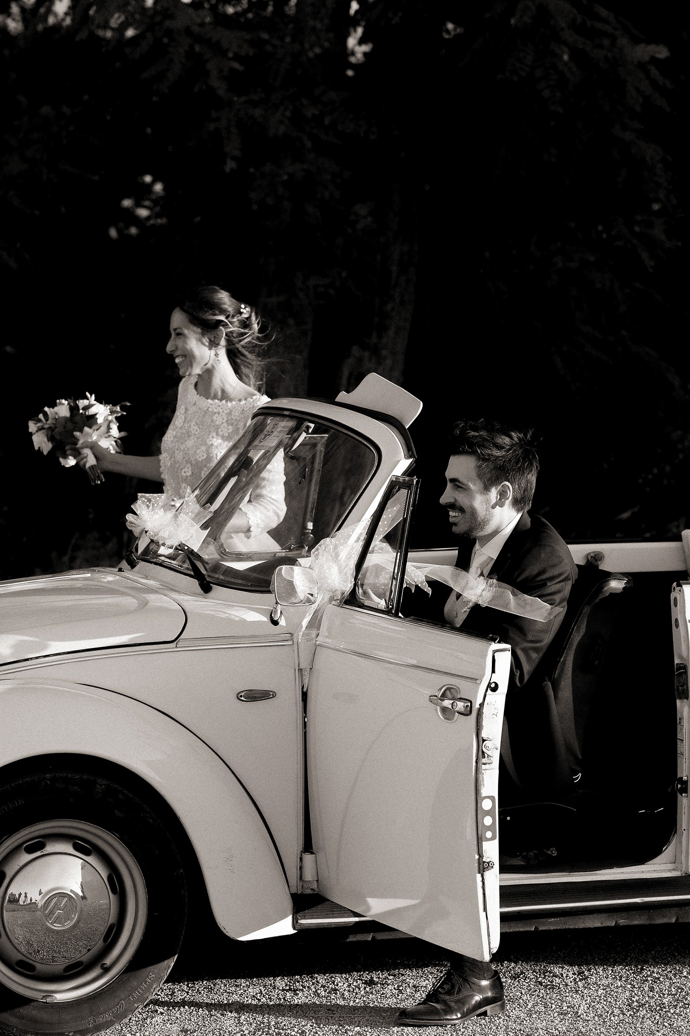Sposi escono da Maggiolino bianco a Villa Peroni Riva, sposa con bouquet, reportage di matrimonio in bianco e nero
