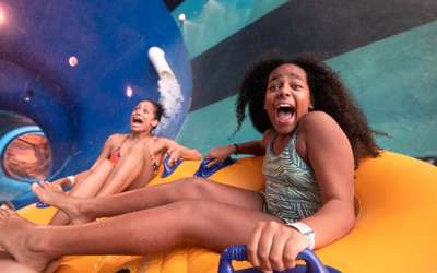 Mother and daughter going down on inflatable tubes on water slide tunnel.