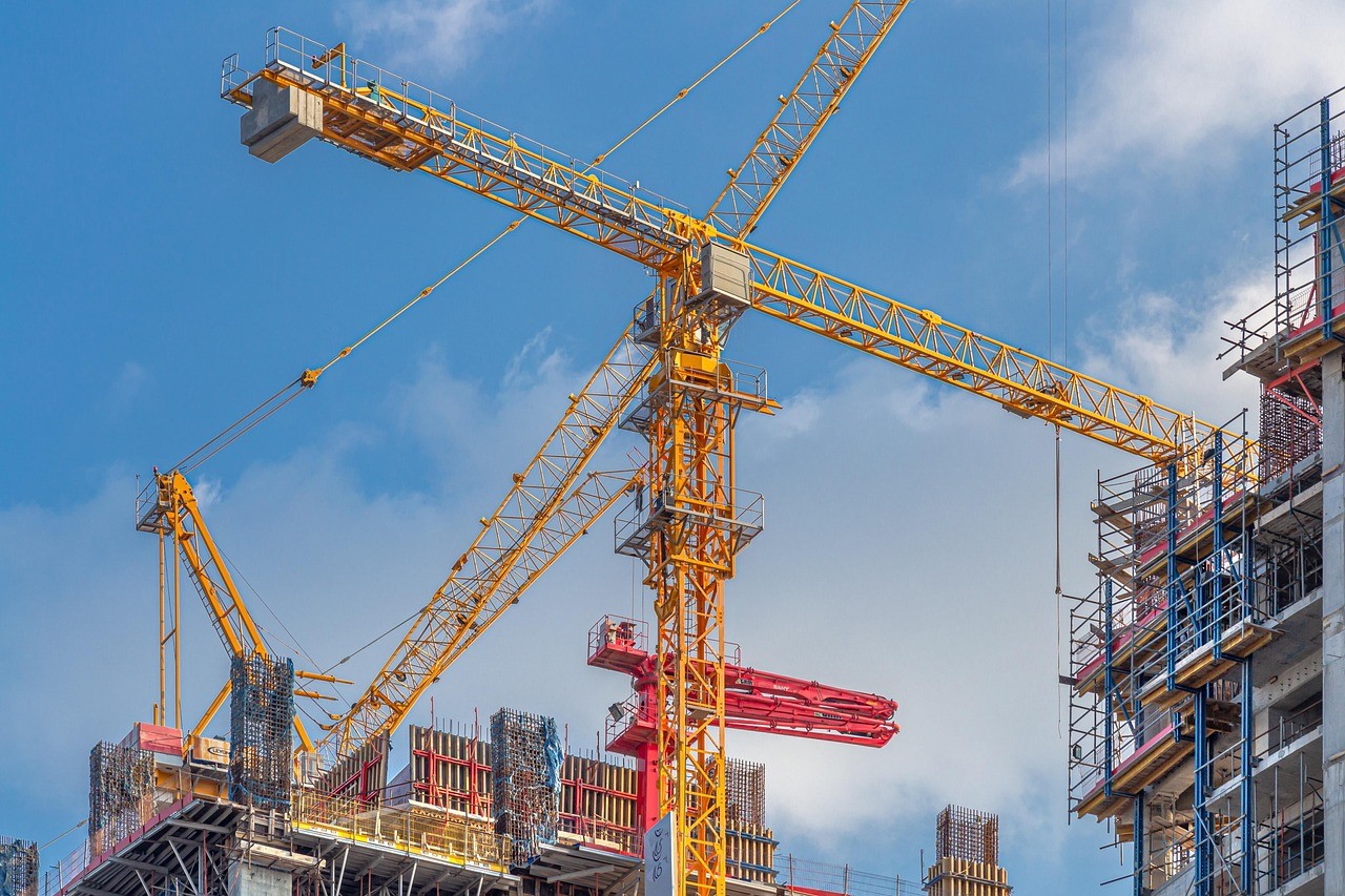 Yellow construction cranes towering over a partially built skyscraper against a clear blue sky, conveying progress and industrial development.