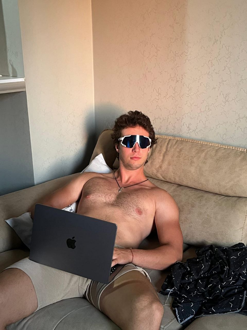 Asian man with glasses in a creative workspace, surrounded by colorful abstract art and stationery on a cluttered desk.