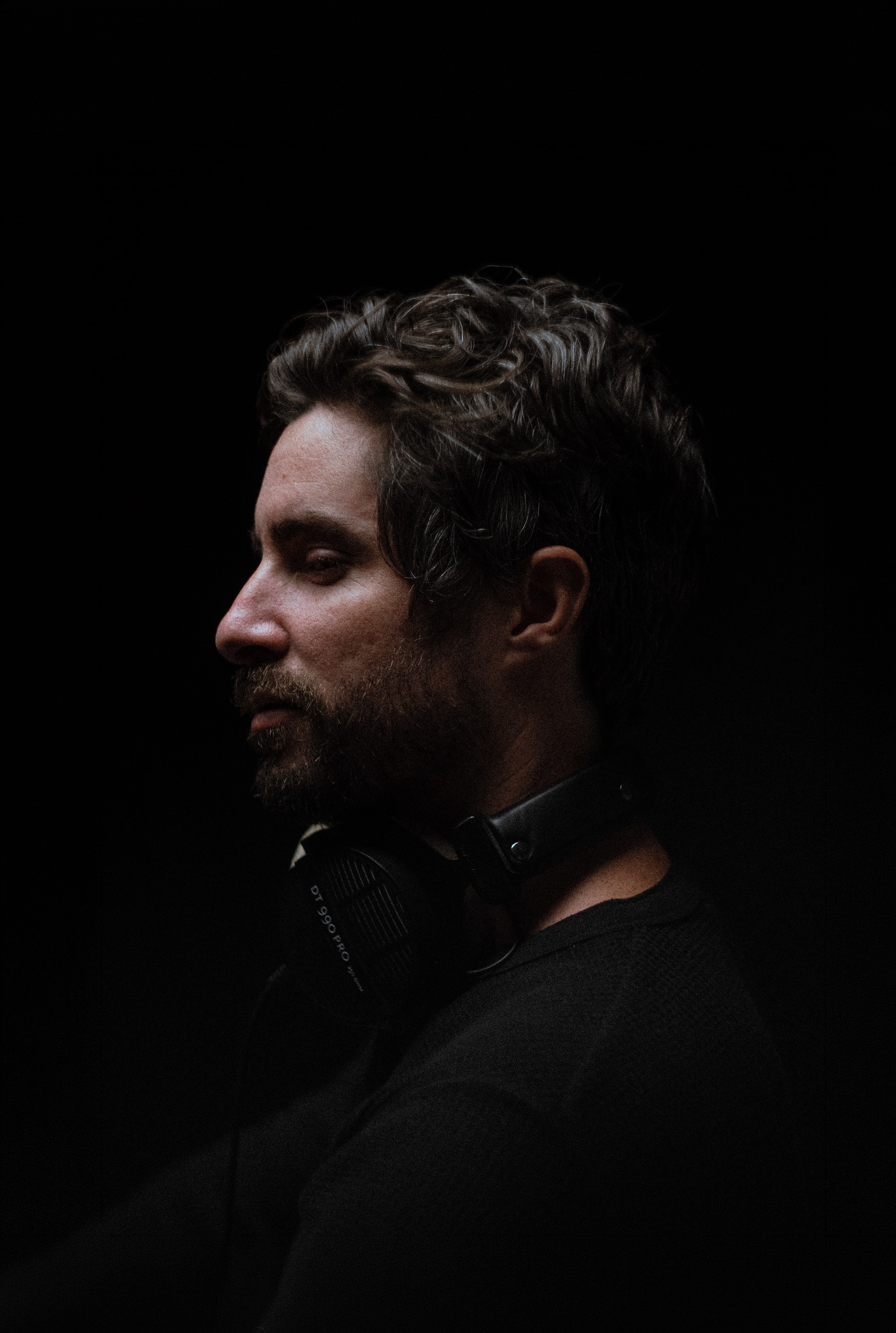 Close-up portrait of a person wearing a gray insulated hooded jacket with the hood up, showing their face framed by the hood against a light background.