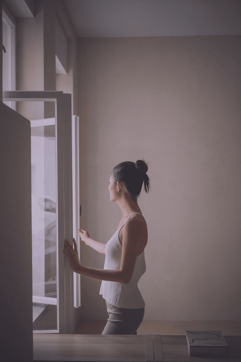 Person gazing out the window in a tank top