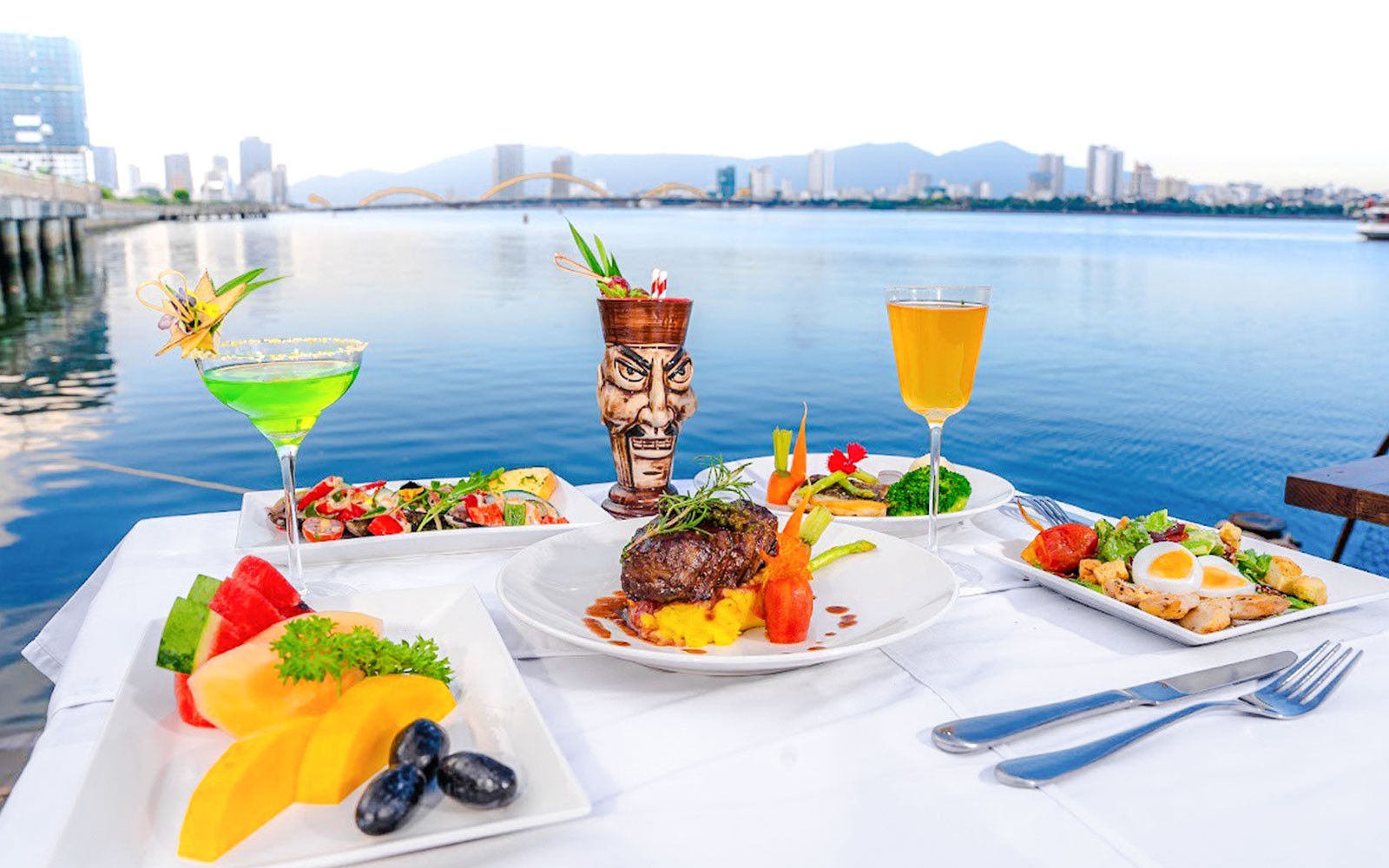 Dining setup on Da Nang Poseidon cruise with city skyline and Dragon Bridge view.