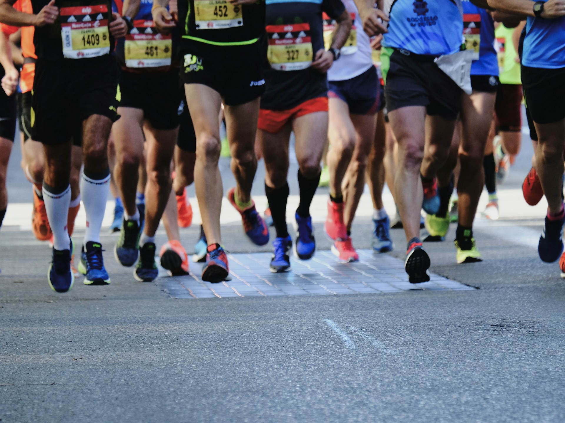 A large group of runners compete in a marathon on a paved road, showing mostly legs and bib numbers.