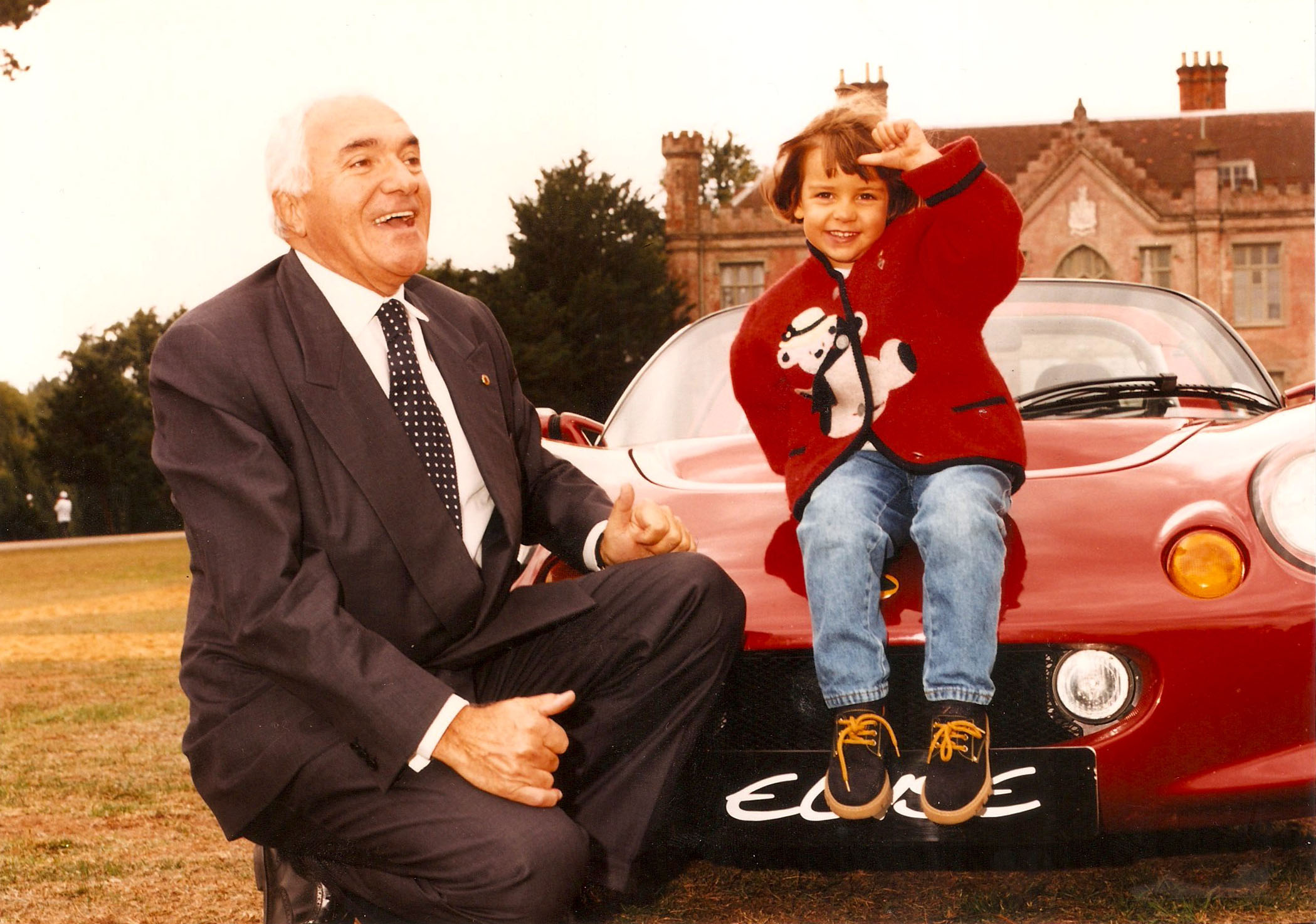 Romano Artioli and his granddaughter Elisa pose in front of a red Lotus Elisa, the sports car named in her honor.