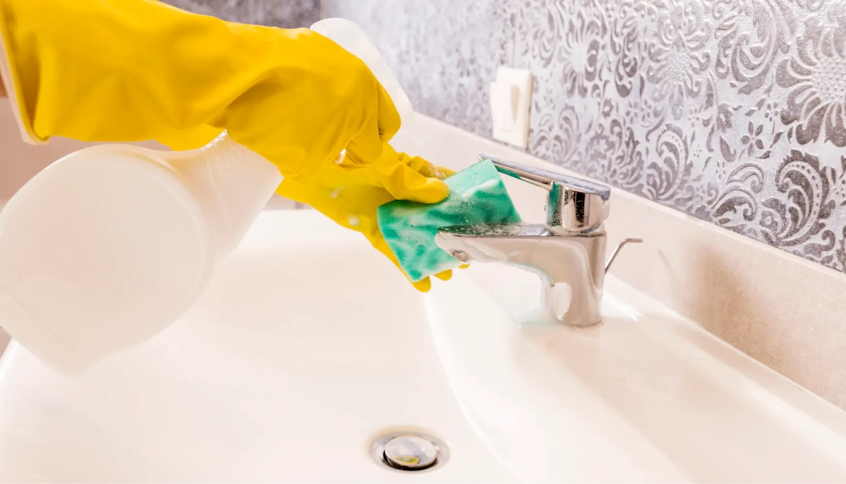 Cleaner wearing yellow gloves scrubbing bathroom sink and faucet with sponge, Midleton