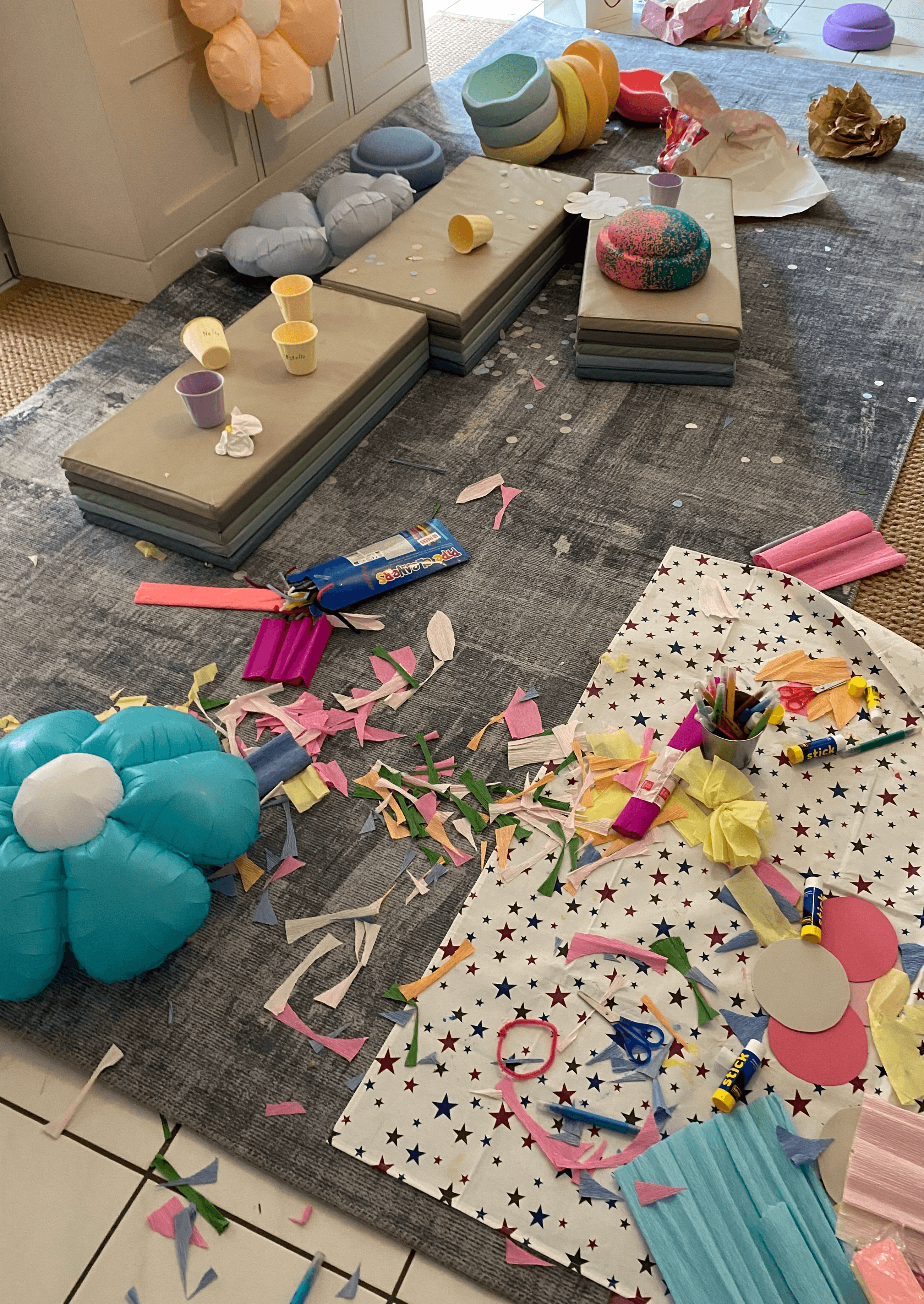 Kinderzimmer nach einem Kindergeburtstag. Totales Chaos. Es liegen Blumenluftballons, bunte Stapelsteine, Papierschnipsel, umgekippte Becher, jede Menge Stifte, Scheren, Bastelmaterial
