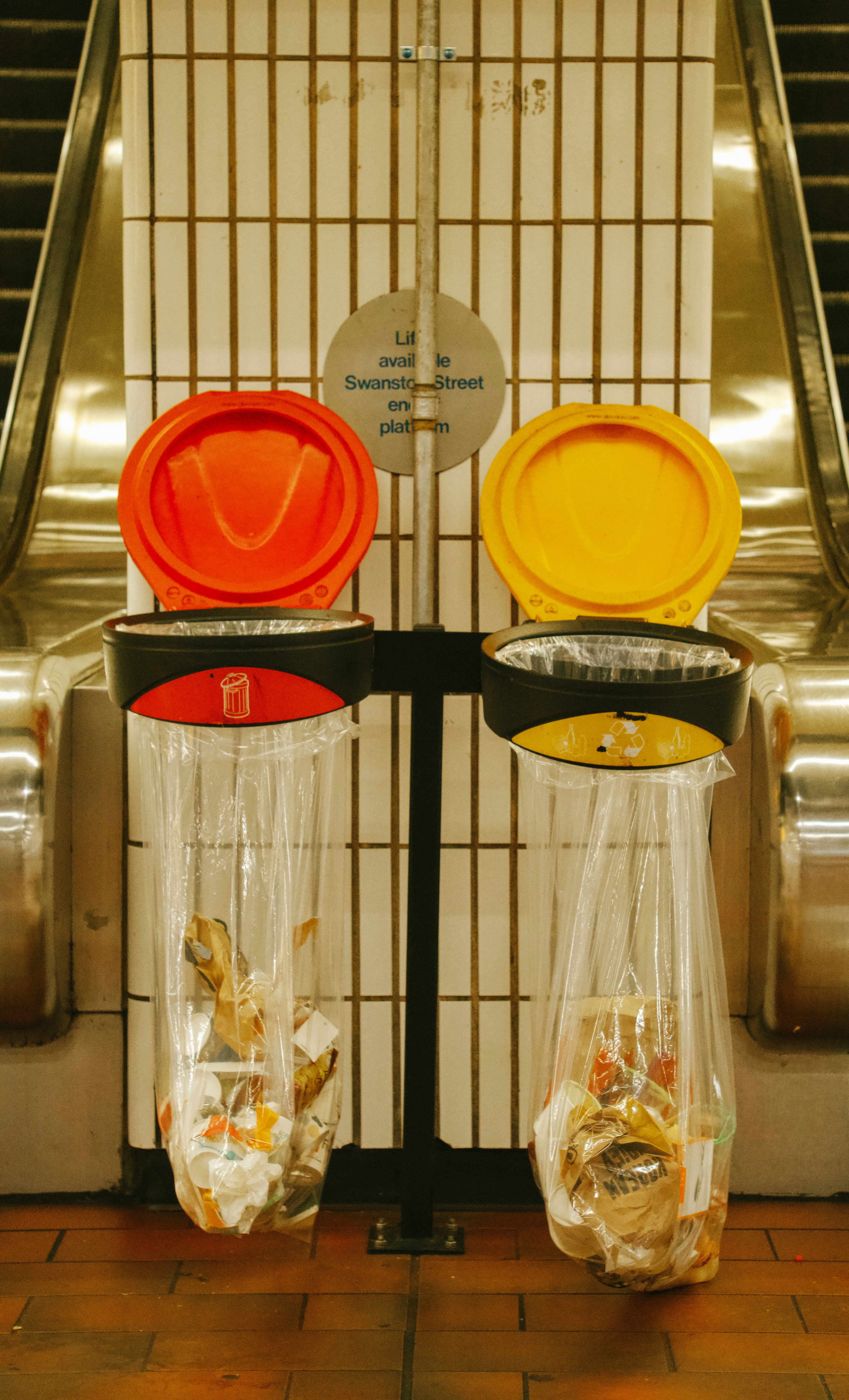 Two colorful trash cans at a subway station.