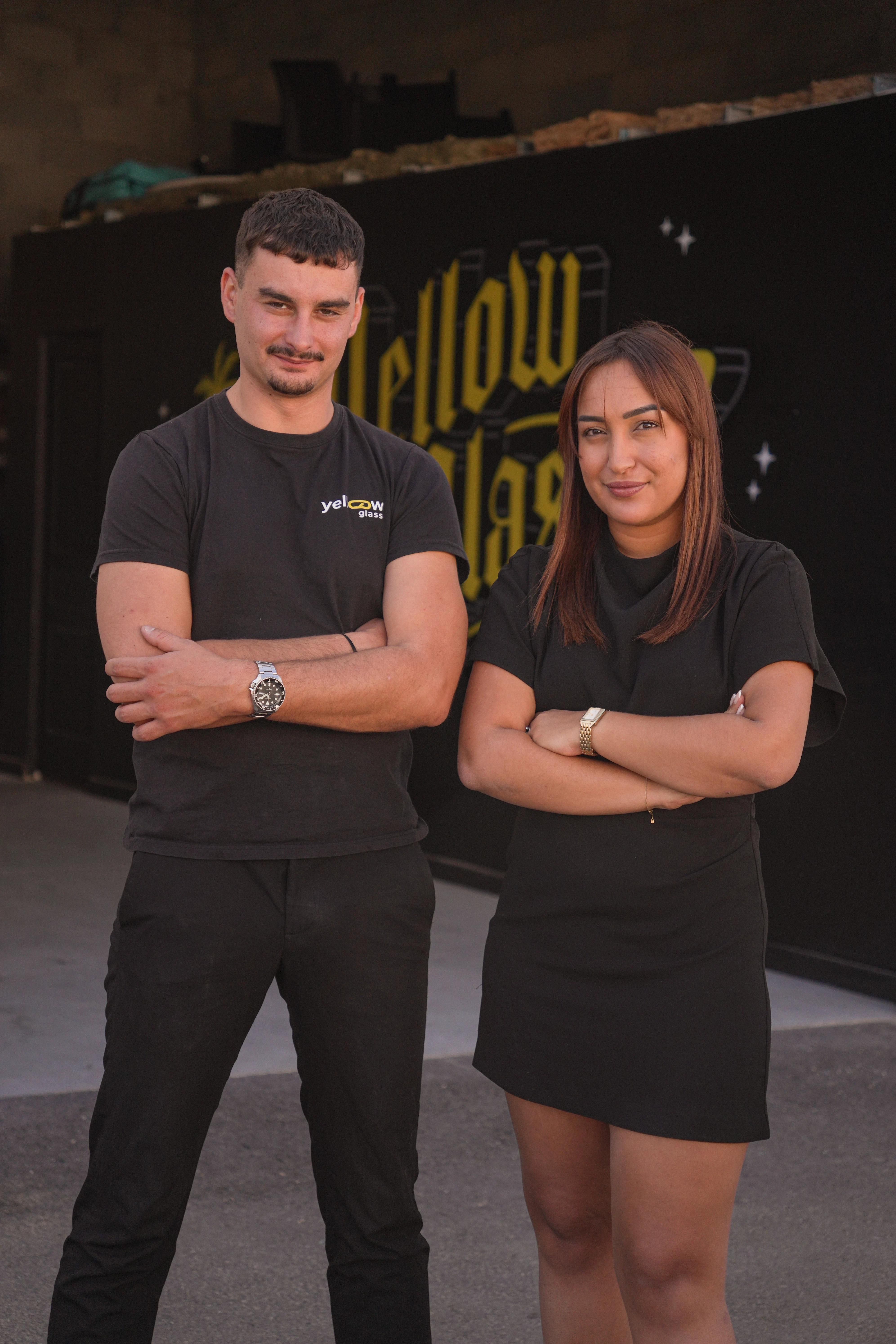 Homme et femme souriants devant un mur avec le mot "Yellow Glass"