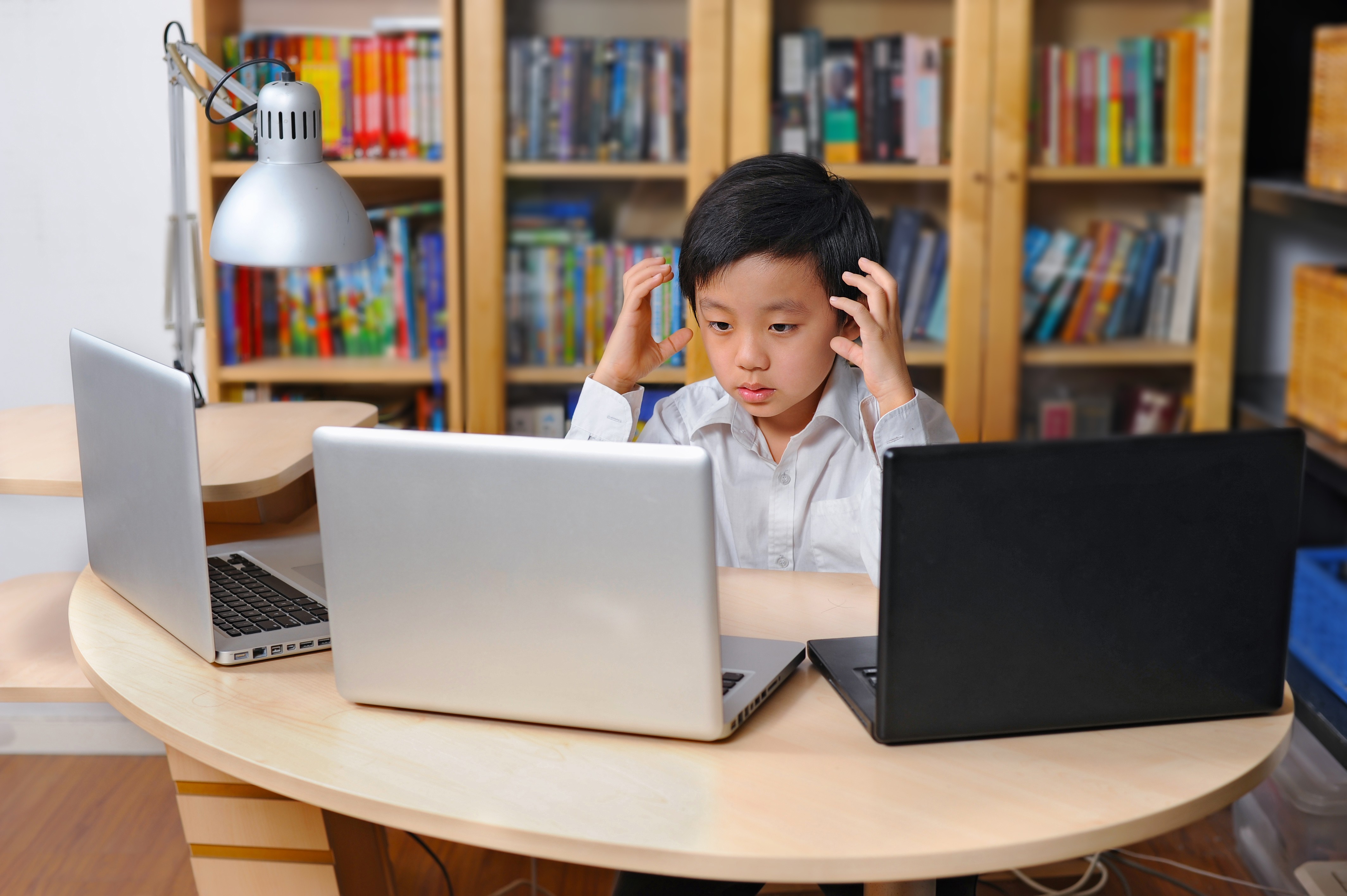 A child struggles with 3 laptops in school