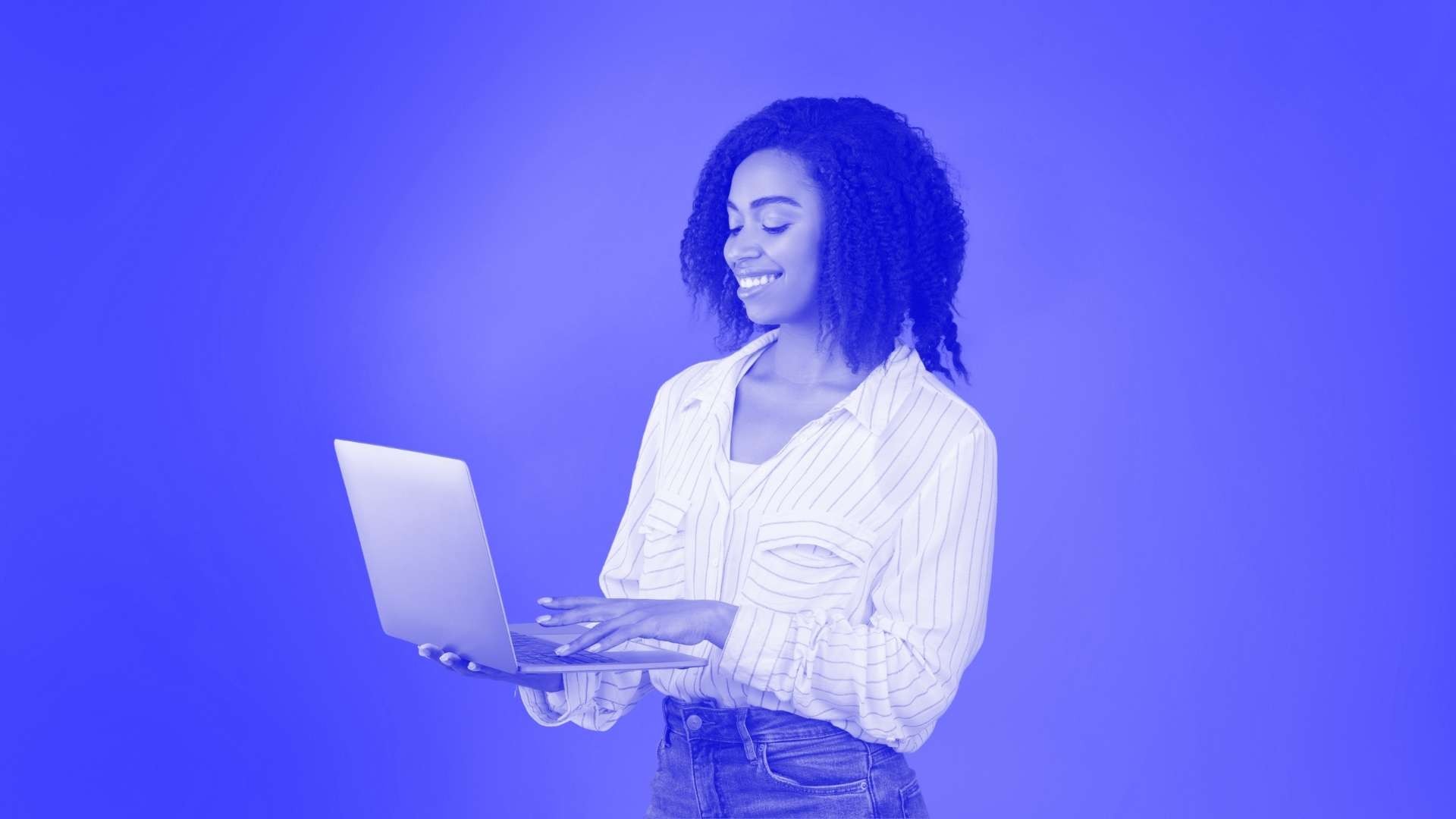 A woman standing up typing on her laptop with one hand