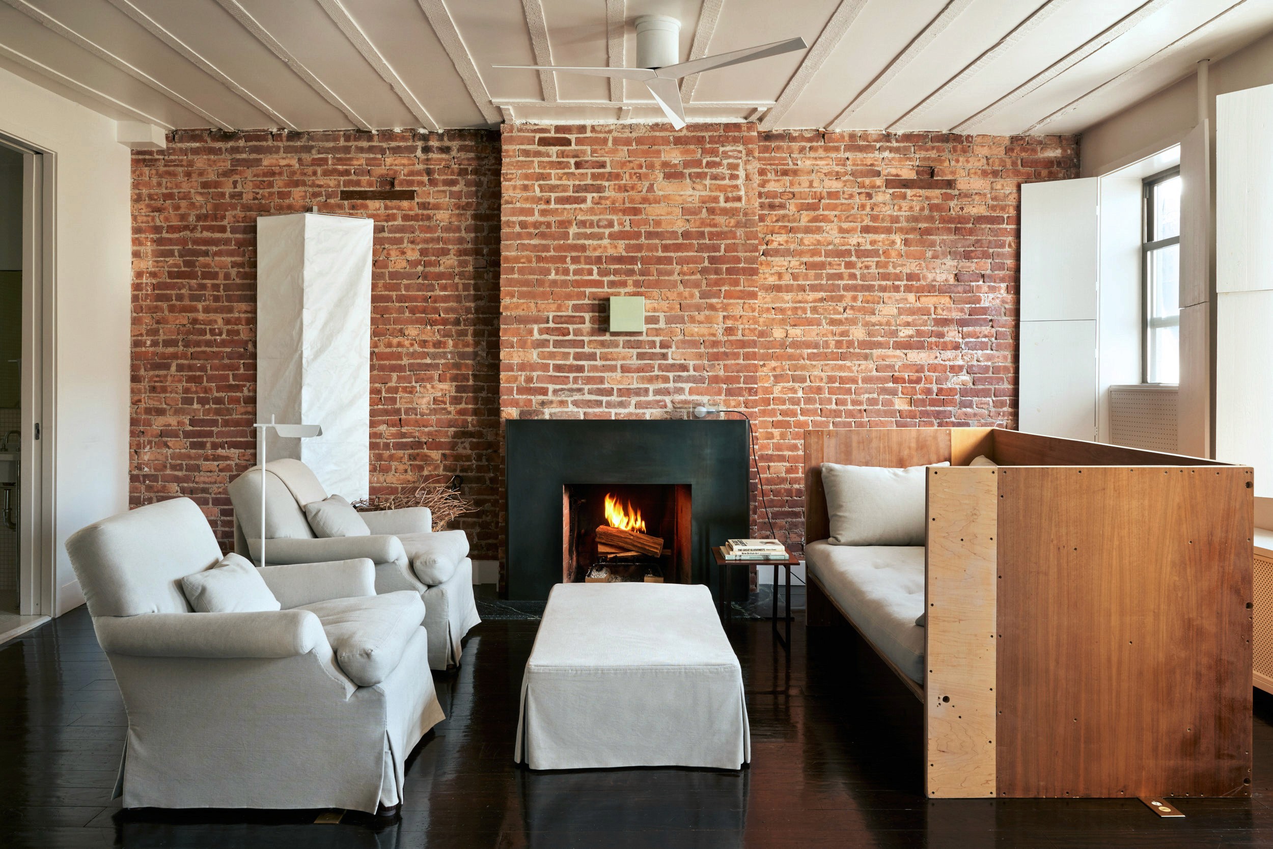 Living room with dark metal fireplace, minimalist wooden sofa, and matching custom upholstered armchairs.