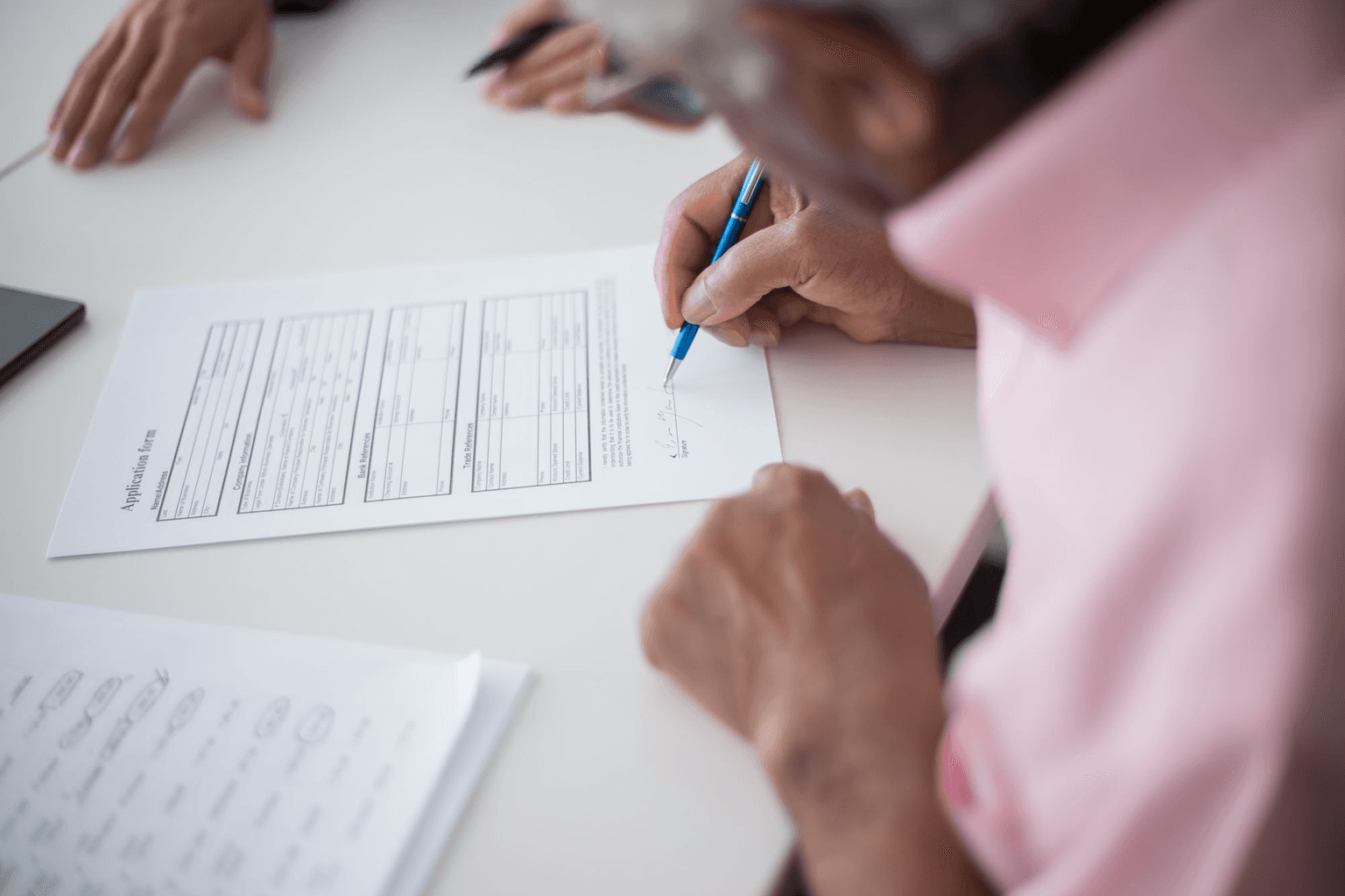 An older person filling in an application form at a table, pen in hand.