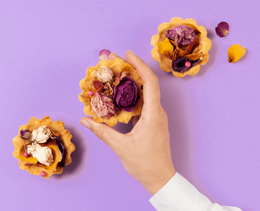  A hand holds a delicate baked tartlet shell filled with assorted dried purple