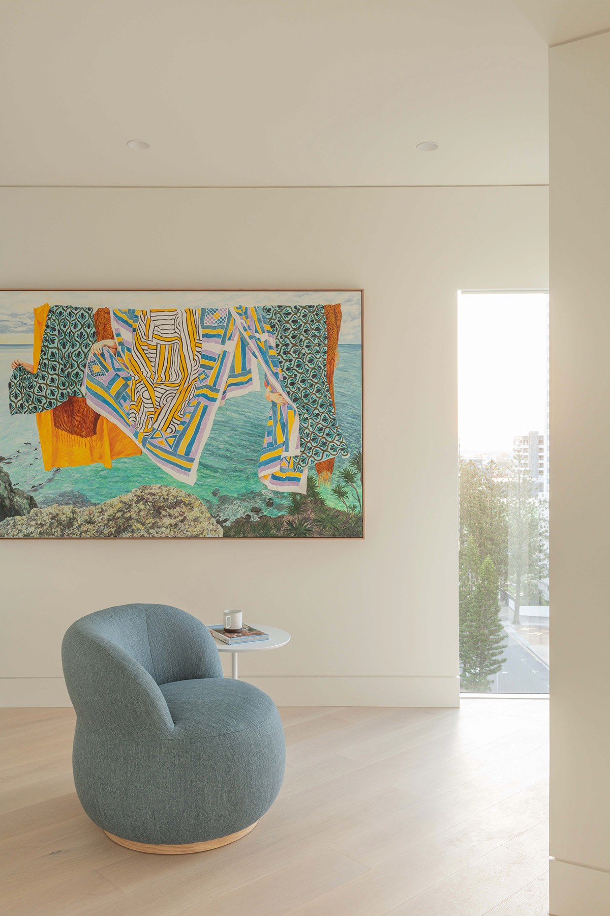 High Tide apartment sitting area with sculptural lounge chair, curated artwork, and natural light overlooking coastal city views.