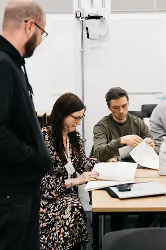 People looking at papers in a classroom with one person writing and another reading.